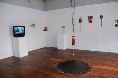 The Chinese Horoscope Show at Enjoy. On floor, Tiffany Singh, Never Follow a Straight Line, 2012, dirt, horse shoes, horse hair, painted bamboo wind chime.  On back wall on the right, Kate Woods, Untitled, 2012, photographs, fringing.