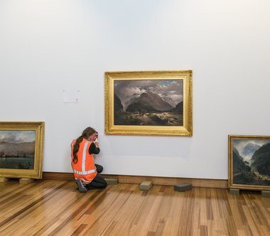 Staff install John Gibb’s Clearing up after rain, foot of Otira Gorge, 1887, oil on canvas. Purchased, 1964. Photograph by John Collie, Christchurch Art Gallery, Te Puna o Waiwhetu